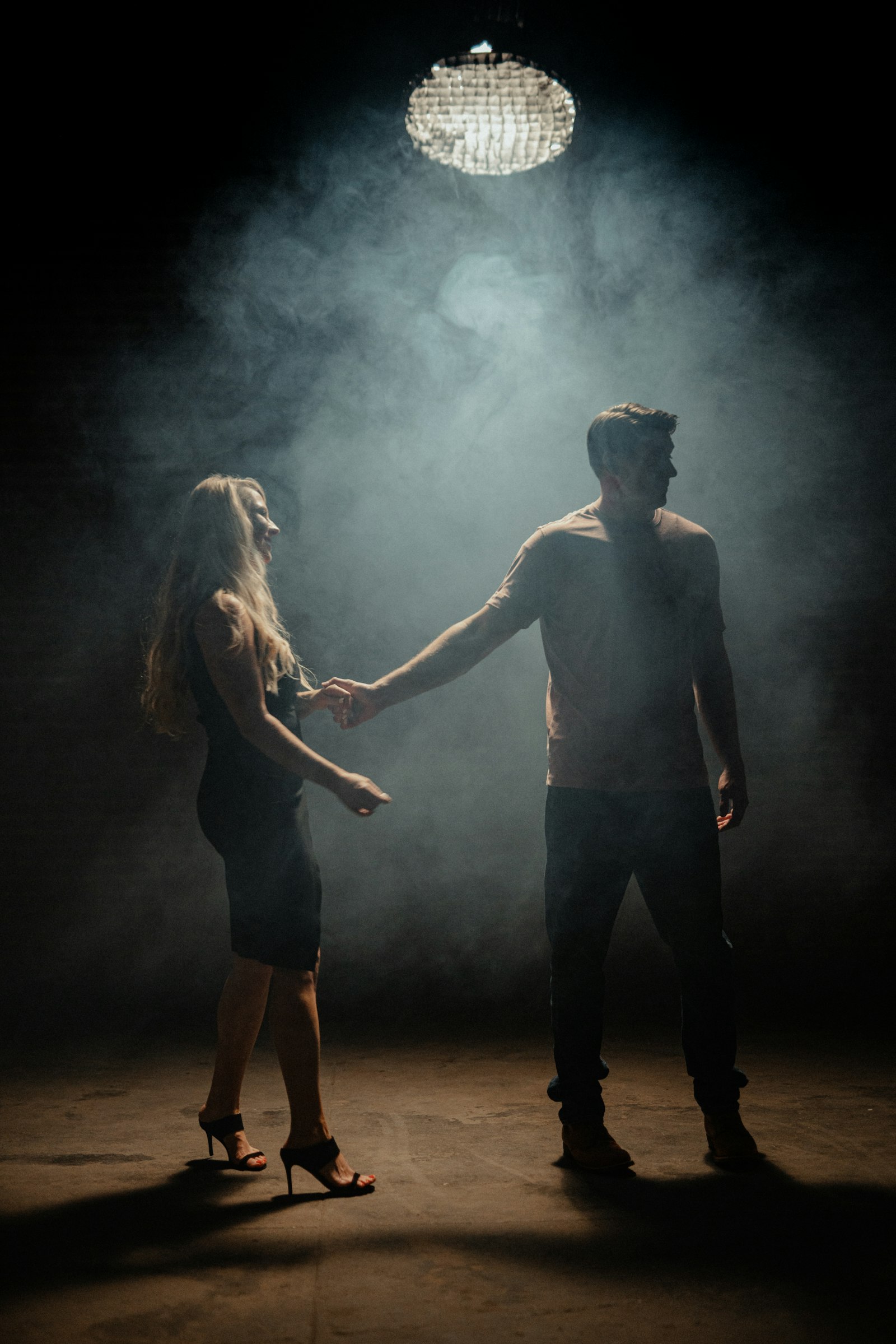 Pareja bailando bajo un haz de luz en un salón oscuro con humo